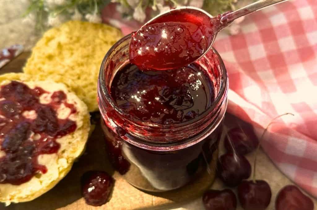 vanilla cherry jam in a Mason jar with a spoon next to a biscuit